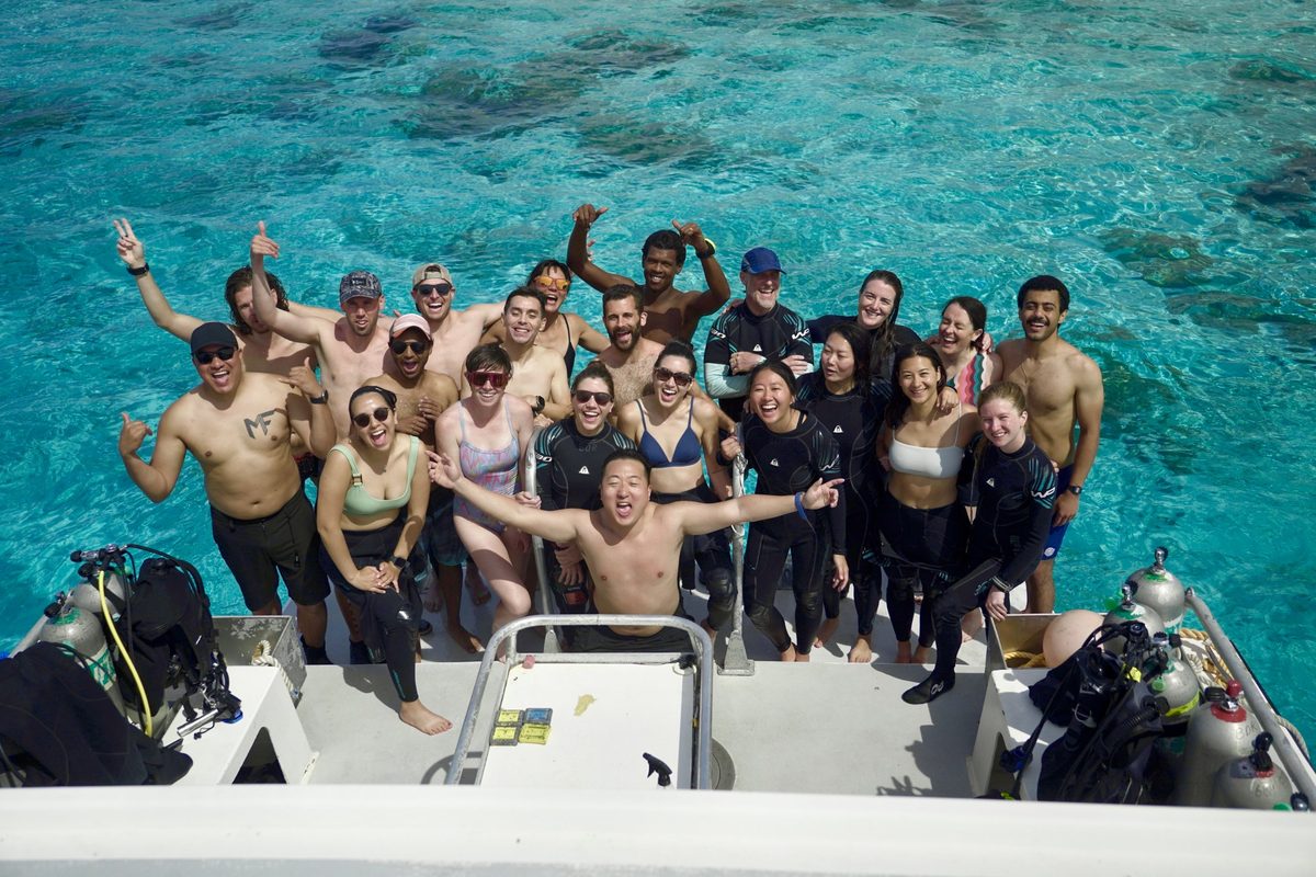The beta testing group cheering on the back of a dive boat over turquoise water