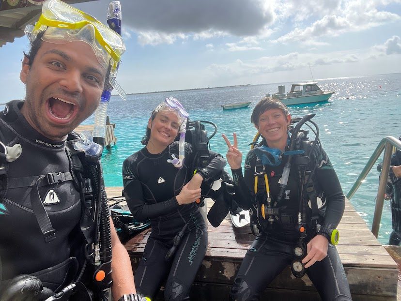 Three divers in wetsuits mugging for a selfie on a dock in Bonaire